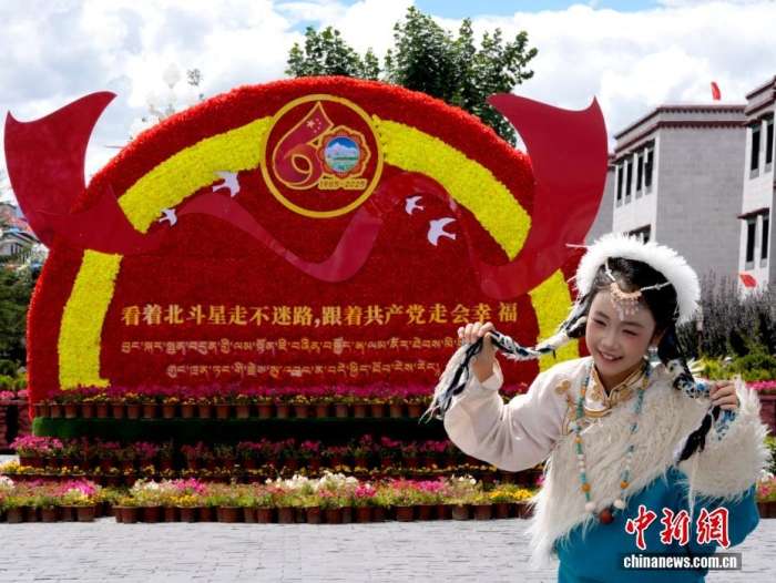 8月19日，随着西藏自治区成立60周年庆祝活动临近，拉萨氛围浓。拉萨街头，处处是张灯结彩的盛景，洋溢着一派祥和与欢腾的氛围。图为游客在拉萨大昭寺广场上的大庆宣传标语前留念。中新社记者李林摄